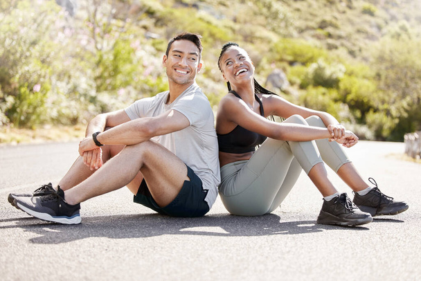 Health, fitness and friends relax after workout in nature, sitting and talking in a road outdoors. Rest, wellness and conversation with diverse man and woman taking a break together after cardio run. - Photo, Image