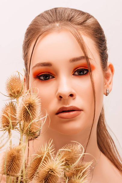 The girl holds dried flowers near her face. Portrait of a young beautiful girl with bright makeup and dried flowers - Foto, Imagem