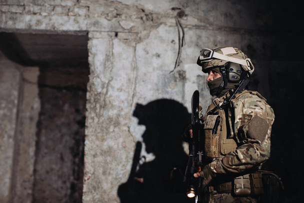 Muotokuva ukrainalaisesta puolustajasta. Aseistettu sotilas heittää varjon seinälle.. - Valokuva, kuva
