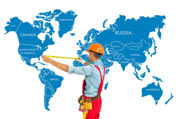 Pracovník v pevném klobouku opatření s pravítkem svět mapa pozadí. - Fotografie, Obrázek