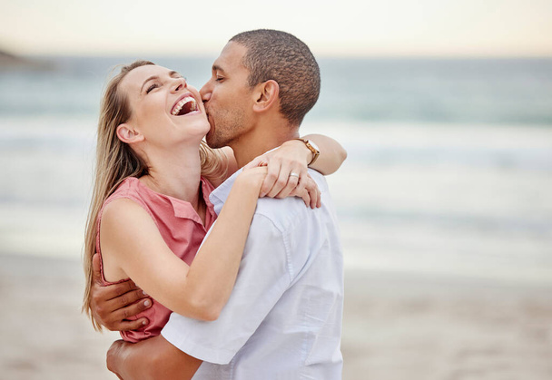 Beach couple love, hug and kiss for summer vacation, happy marriage and lifestyle together. Laughing woman, playful man and interracial relationship enjoying ocean travel, holiday break and happiness. - Foto, Imagen