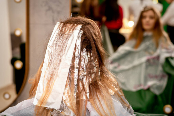 Mooie jonge blanke vrouw met folie in haar haar, terwijl het verven van haar haar zitten in een schoonheidssalon - Foto, afbeelding