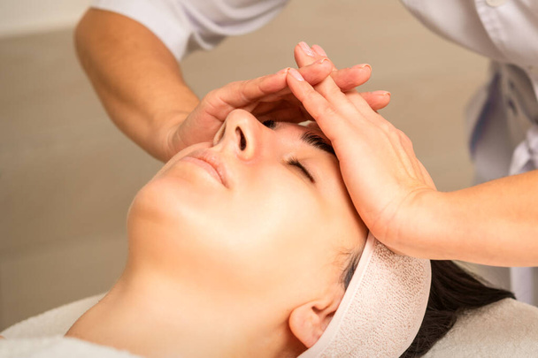 Massagem facial. Jovem caucasiana com os olhos fechados recebendo uma massagem na testa em um salão de beleza - Foto, Imagem