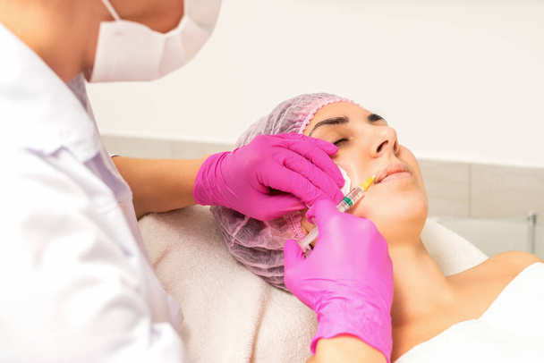 Молодая белая женщина получает инъекцию ботокса с гиалуроновой кислотой в губы в клинике красоты - Фото, изображение