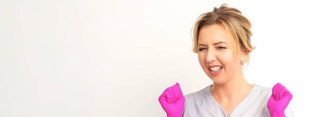 Happy caucasian woman doctor wearing pink gloves celebrates and raising fists on white background - Photo, image