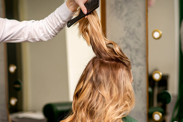 Professionele haarverzorging. jong vrouwelijk blond met lang haar ontvangst hairstyling in een schoonheidssalon - Foto, afbeelding