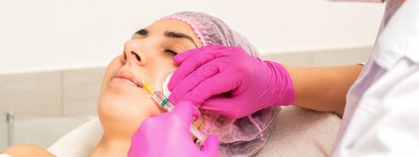 Młoda kobieta rasy kaukaskiej otrzymuje wstrzyknięcie botoksu kwasem hialuronowym w usta w klinice kosmetycznej - Zdjęcie, obraz