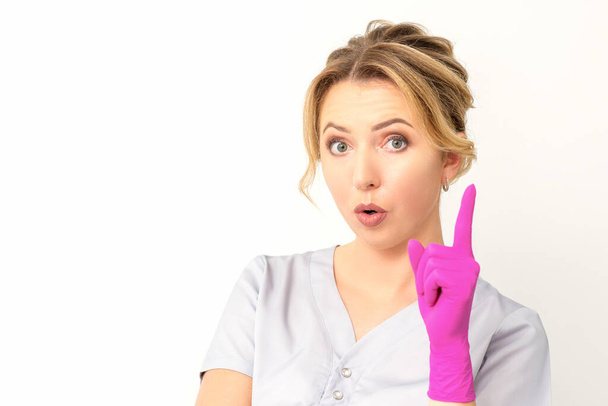 Jonge blanke vrouw arts draagt roze handschoenen houden wijsvinger naar boven gericht maken van een gebaar met wijsvinger. Ik heb een idee. - Foto, afbeelding