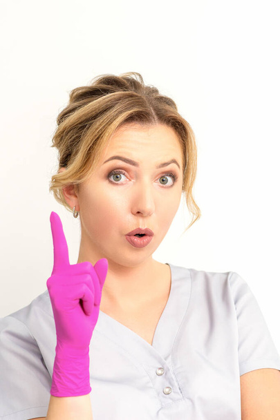 Молодая белая женщина-врач в розовых перчатках, указывая указательным пальцем вверх, делает жест указательным пальцем. У меня есть идея. - Фото, изображение