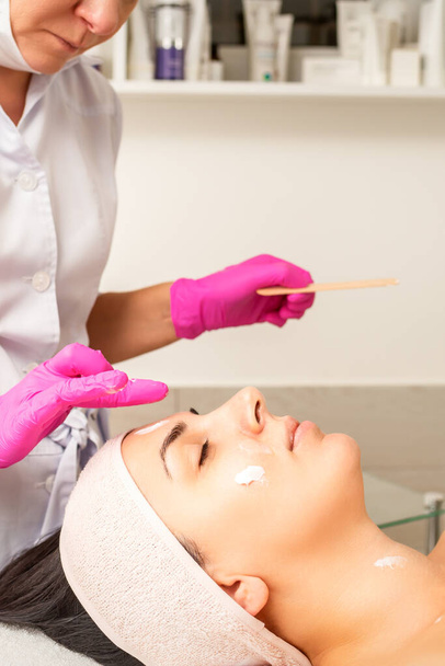 手袋をはめた手で美容師は女性の顔にクリームを剥離と保湿マスクを適用します。顔の美容治療.フェイシャルケアの手順 - 写真・画像