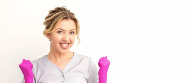 Happy caucasian woman doctor wearing pink gloves celebrates and raising fists on white background - Foto, afbeelding