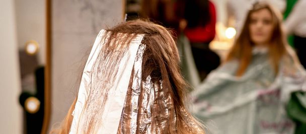 Saçında folyo olan güzel beyaz bir kadın bir güzellik salonunda otururken saçını boyuyor. - Fotoğraf, Görsel