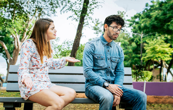 Αναστατωμένο ζευγάρι να μαλώνει σε ένα πάρκο. Κορίτσι υποστηρίζοντας με το φίλο της κάθεται σε ένα πάρκο, Νεαρό ζευγάρι υποστηρίζοντας και διαμαρτύρονται κάθεται σε ένα παγκάκι πάρκο, Έννοια των προβλημάτων ζευγάρι και ζήλια - Φωτογραφία, εικόνα