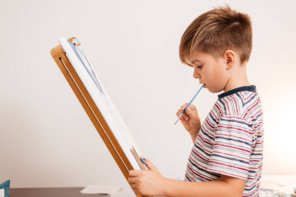 A boy paints a picture on an easel and paints - Foto, imagen