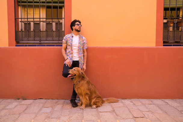 young latin man and his brown golden retriever dog, the man standing up looks at his pet who is sitting on the ground and grabs his head. Pets concept. - Foto, Imagen