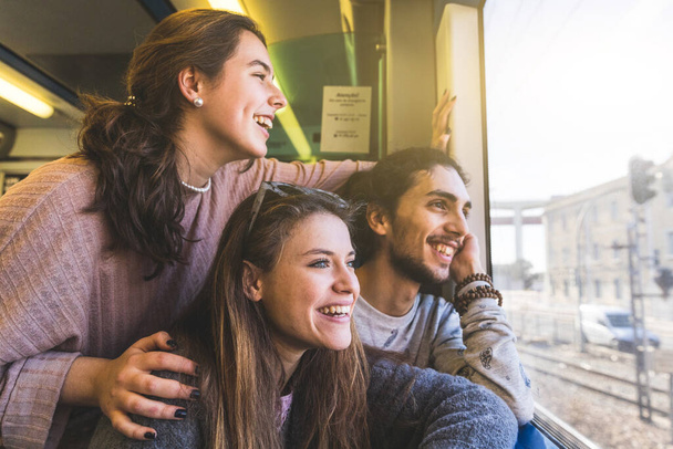 Happy group of friends looking out of train window while travelling on vacation together on a sunny day in Portugal - Smiling young man and women, copy space on the right - Foto, Bild