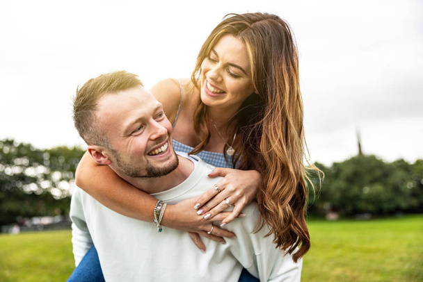 Happy couple having fun and enjoying piggyback ride at park - Candid beautiful caucasian young couple, man and woman - Lifestyle and family concepts - Fotoğraf, Görsel