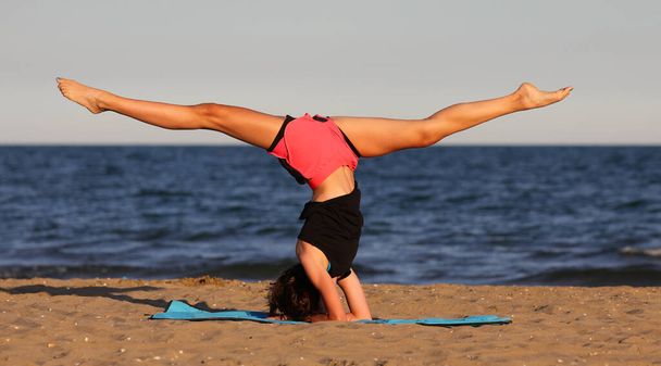 young slender athletic girl does exercises on gym mat on the beach in summer - Zdjęcie, obraz