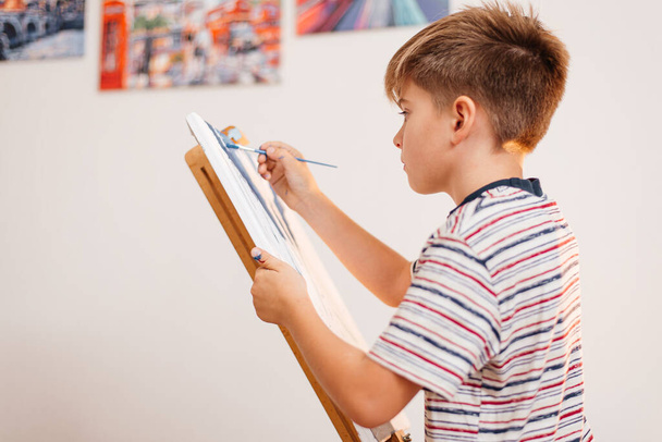A boy paints picture with a brush on an easel - Fotoğraf, Görsel