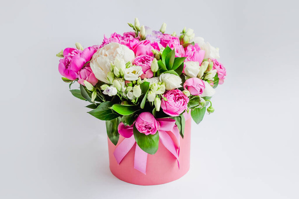 Rozmieszczenie kwiatów w pudełku na kapelusze. Bukiet piwonii, eustoma, spray róża w różowym pudełku z oazą na białym tle - Zdjęcie, obraz