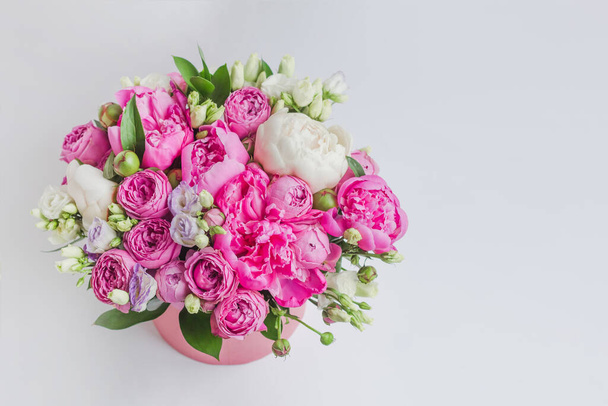 Plaatsing van bloemen in een hoedendoos. Boeket pioenen, eustoma, spray roos in een roze doos met een oase op een witte achtergrond - Foto, afbeelding