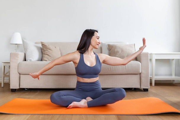 Mulher asiática se exercitando em casa, alongamento. Está na hora do ioga. Jovem atraente e saudável fazendo exercícios enquanto descansa em casa. Jovem se exercitando em casa, interior - Foto, Imagem