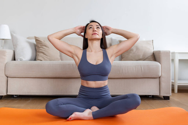 Asiático atraente sorrindo mulher praticando ioga, sentado em Half Lotus exercício, Ardha Padmasana pose, exercitando-se, vestindo sportswear, sessão de meditação, comprimento total interior, casa interior - Foto, Imagem