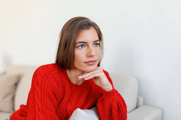 Happy young woman sitting on sofa at home and looking at camera. Portrait of comfortable woman in winter clothes relaxing on armchair. Portrait of beautiful woman smiling and relaxing during autumn. - Photo, Image