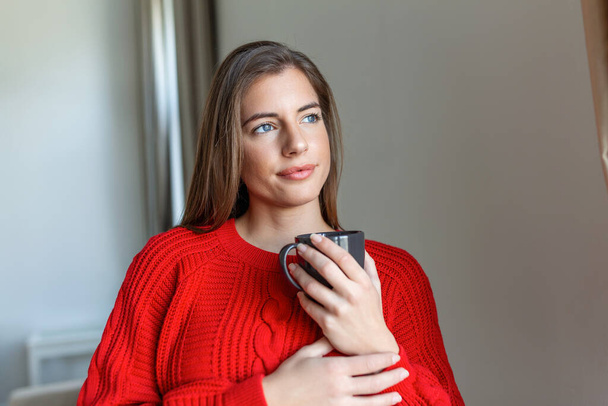 Closeup view of young woman with cup of hot drink at home, blank space. People, drinks and leisure concept - happy young woman with cup of tea or coffee at home - Photo, Image