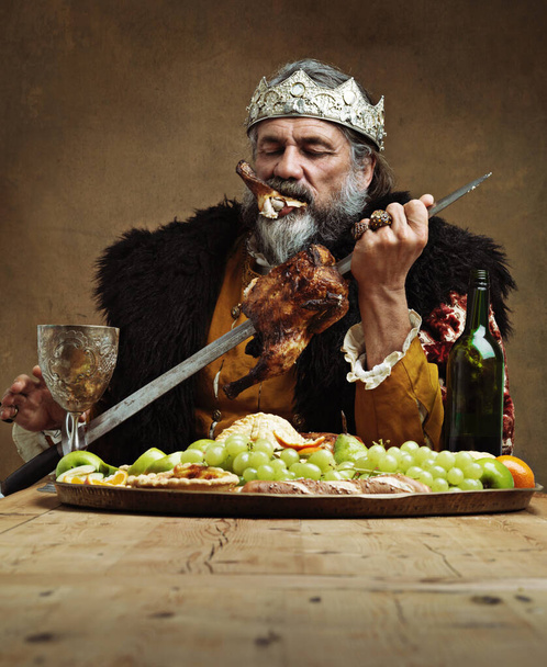 Who needs a knife when you have a sword. A mature king feasting alone in a banquet hall - Fotoğraf, Görsel