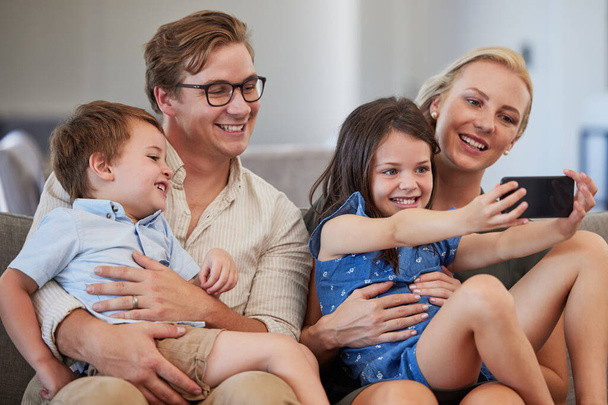 Family selfie, live streaming phone and girl on the internet with technology, smile for mobile app and record video for web on the sofa in living room. Mother and father taking photo with kids. - Valokuva, kuva