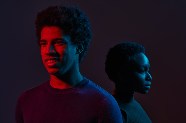 Young man and woman standing together in neon light over dark background, concept of human emotions, facial expression, fashion, beauty - Photo, Image