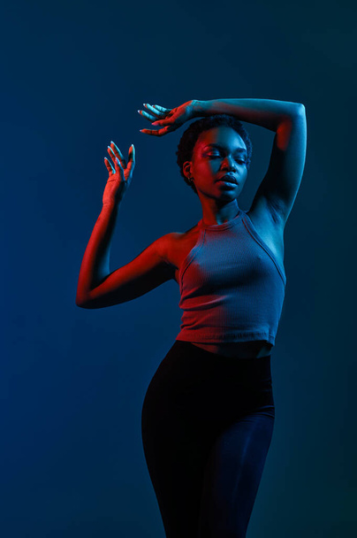 Awesome young slim fashion woman moving gracefully over dark studio background under neon light illumination - Foto, Imagen