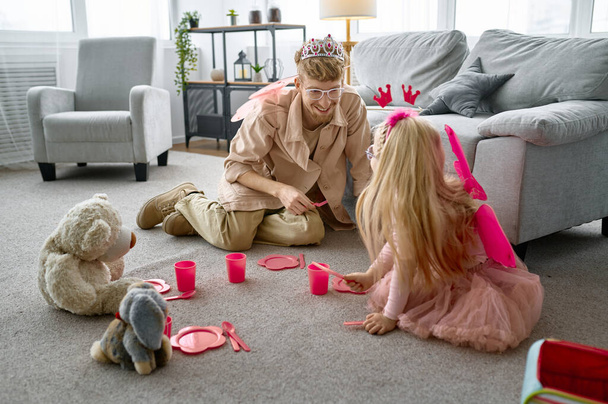 Boldog apa és kislánya viselnek, mint a mágikus tündérek játszik tea party az otthoni nappaliban - Fotó, kép