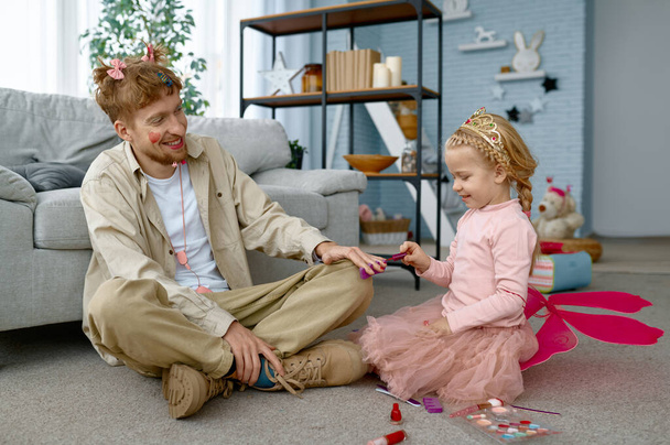 Κόρη ζωγραφική νύχια πατέρα με βερνίκι νυχιών κάνει διαδικασίες ομορφιάς στο σπίτι, αστείο χόμπι - Φωτογραφία, εικόνα