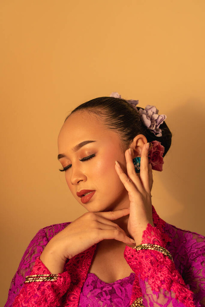 Porträt einer Balinesin mit rosa Kleid posiert mit den Händen auf dem Gesicht im Raum - Foto, Bild