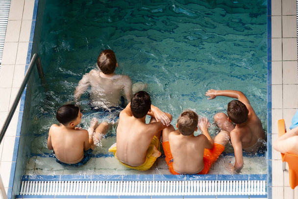 Viele Kinder sitzen mit dem Rücken zum Pool - Foto, Bild