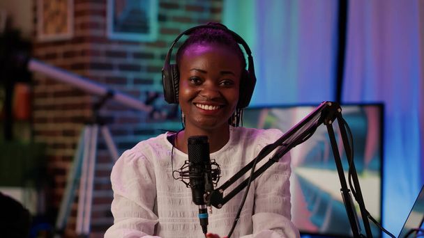 Portrait of online radio host smiling confident at camera while broadcasting live using professional equipment in recording studio. African american podcaster sitting at desk with boom arm microphone. - Photo, Image