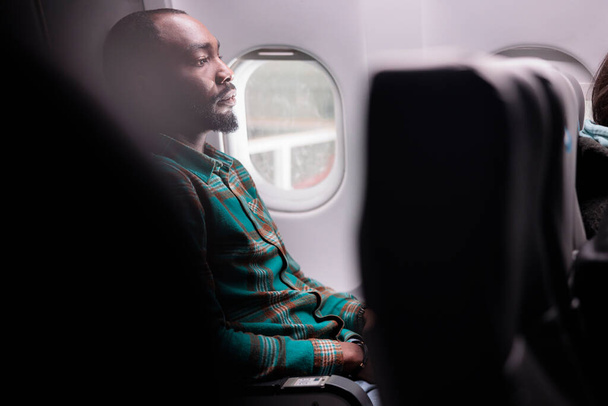 African american tourist flying in economy class with airplane to leave on business work trip. Freelancer travelling abroad with international airways, using plane transportation. - Photo, Image