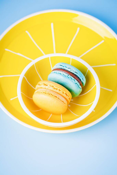 Blue and yellow macaron on a yellow plate and a blue background, copy space - Foto, immagini
