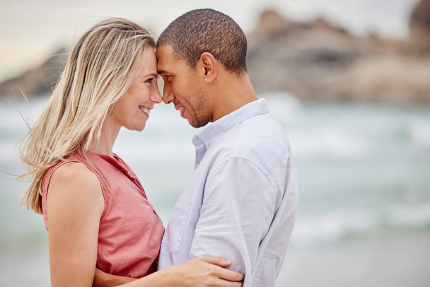 Interracial couple, beach and love bond with forehead together in trust, security or safety. Smile, happy or latino man and woman in hug by ocean or sea water in nature environment for honeymoon date. - Photo, Image