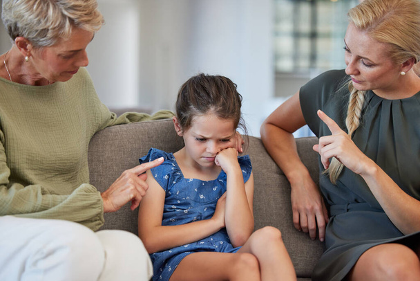 Family, discipline and warning by mother and grandmother hand sign to girl for bad behaviour on a sofa at home. Autism, adhd and communication by parent and daughter in conflict with attitude problem. - Foto, Imagen