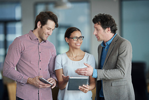 Poner en práctica sus planes. un grupo de compañeros de trabajo de pie en una oficina hablando por una tableta digital - Foto, imagen