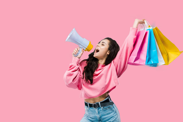 Big sales concept. Black friday. Happy trendy pretty caucasian young woman, in casual clothes, holding shopping bags, says announcement in loudspeaker, posing on isolated pink background - Photo, Image