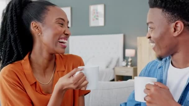 Gelukkig zwart echtpaar met een kopje koffie op een bank om te ontspannen en uit te rusten in de slaapkamer van een modern huis. Glimlach, liefde en Afrikaanse man en vrouw zitten, praten en lachen samen op een bank thuis - Video