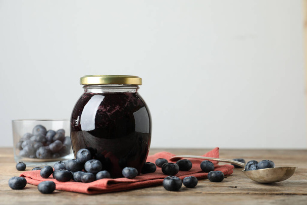 Jar of blueberry jam and fresh berries on wooden table. Space for text - Valokuva, kuva