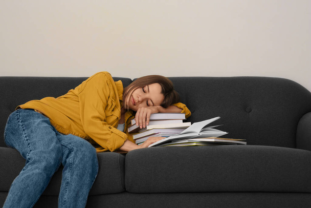 Young tired woman sleeping near books on couch indoors - Foto, Imagen