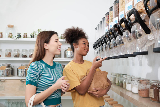 Zwei glückliche junge Kundinnen entscheiden sich für Bioprodukte im Refill-Store mit Mehrwegtaschen, abfallfreien Lebensmitteln und einem plastikfreien, umweltfreundlichen und nachhaltigen Lebensstil.. - Foto, Bild