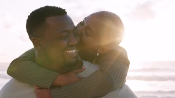 Plage, amour et un piggyback, un couple heureux baiser à la mer pendant le coucher du soleil. Une femme et un homme noirs, un sourire et une soirée romantique à l'océan. Vagues, sable et romance, vacances d'été le soleil africain - Séquence, vidéo