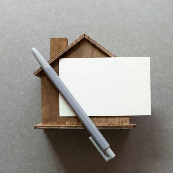 Modelo de casa de madera y bloc de notas en blanco sobre fondo gris. Concepto inmobiliario. vista superior, espacio de copia - Foto, Imagen